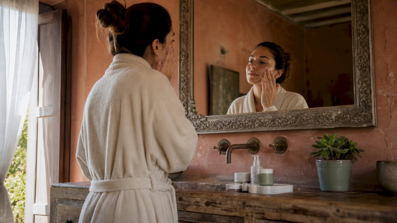 Woman applying moisturizer in bathroom