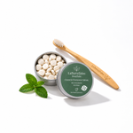 LaTerraTales DentTabschewable toothpaste tablets in an open silver tin, shown with a bamboo toothbrush and mint leaves on a white background.