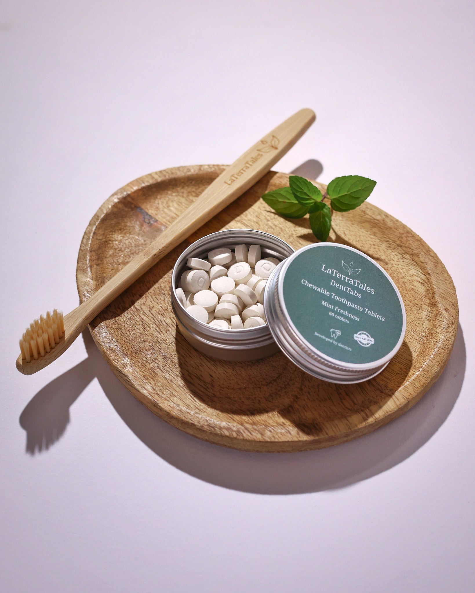Bamboo toothbrush, wooden plate with dental tablets, and a container labeled 'LaTerraTales' on a light background.