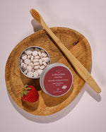 LaTerraTales dental product with a wooden toothbrush and strawberry on a wooden plate.