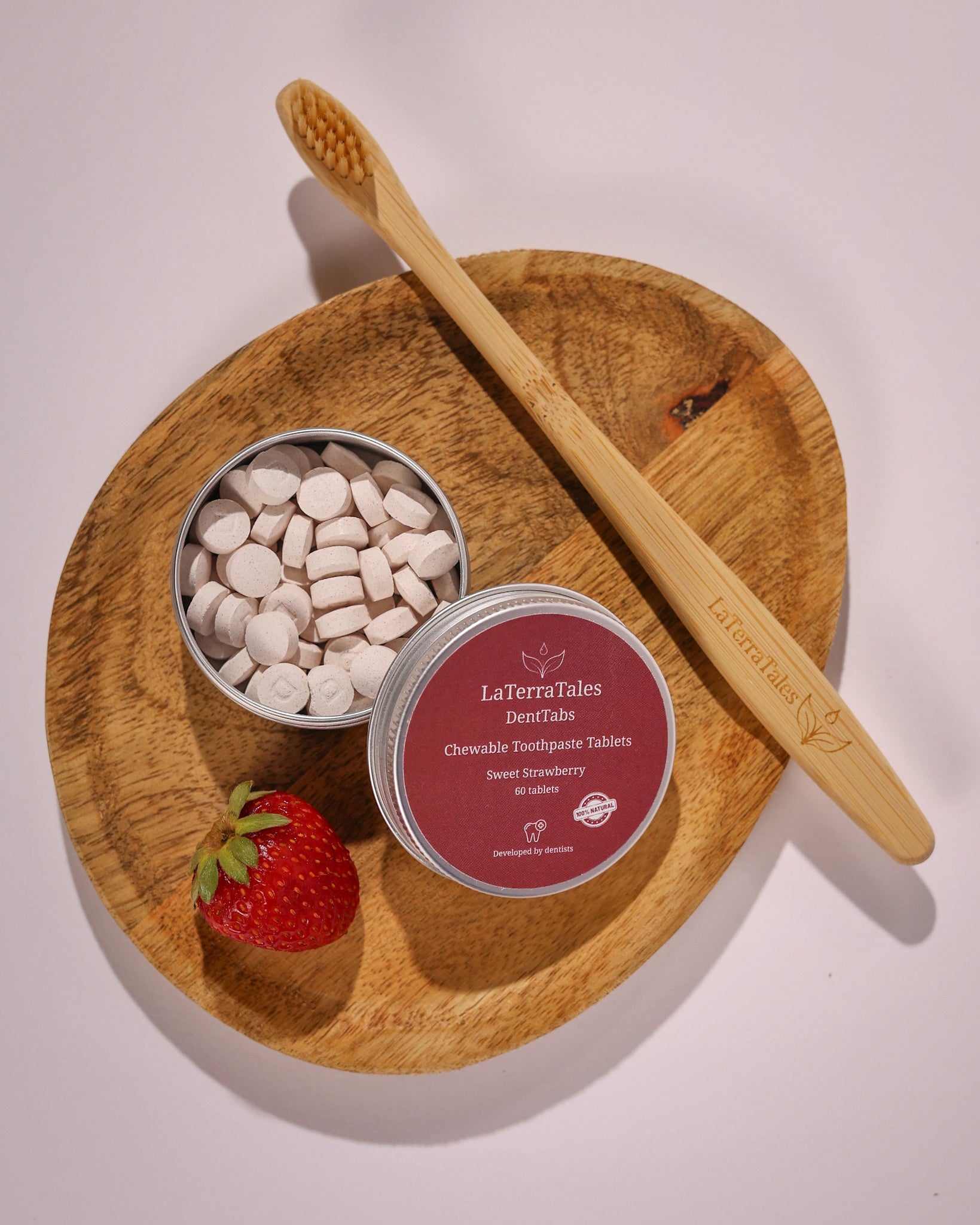 LaTerraTales dental product with a wooden toothbrush and strawberry on a wooden plate.